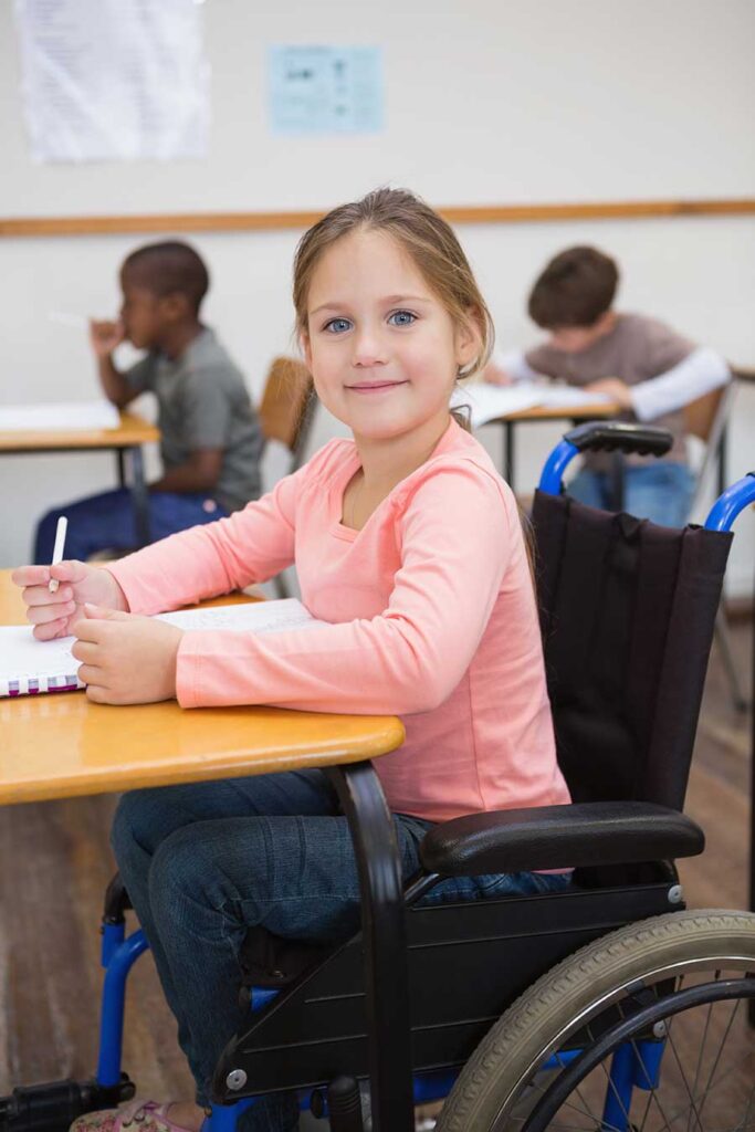 Young girl in wheelchair in school, looking at camera