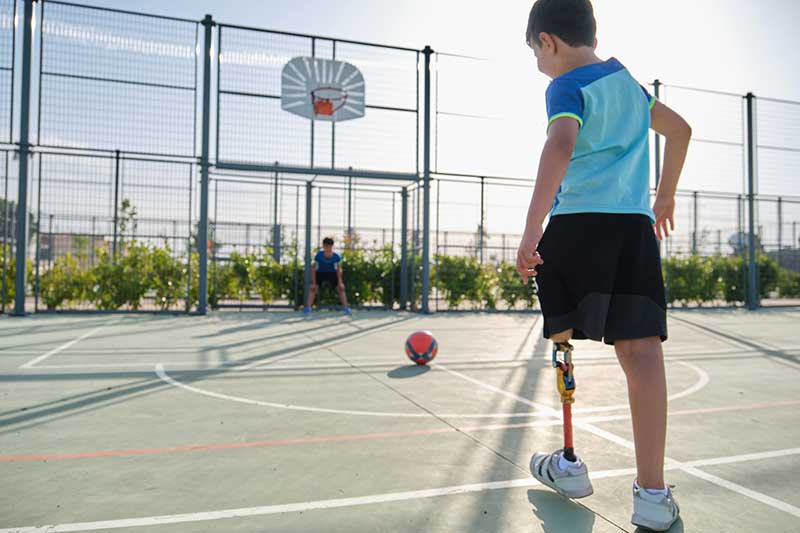 boy with leg prosthesis playing ball on a court