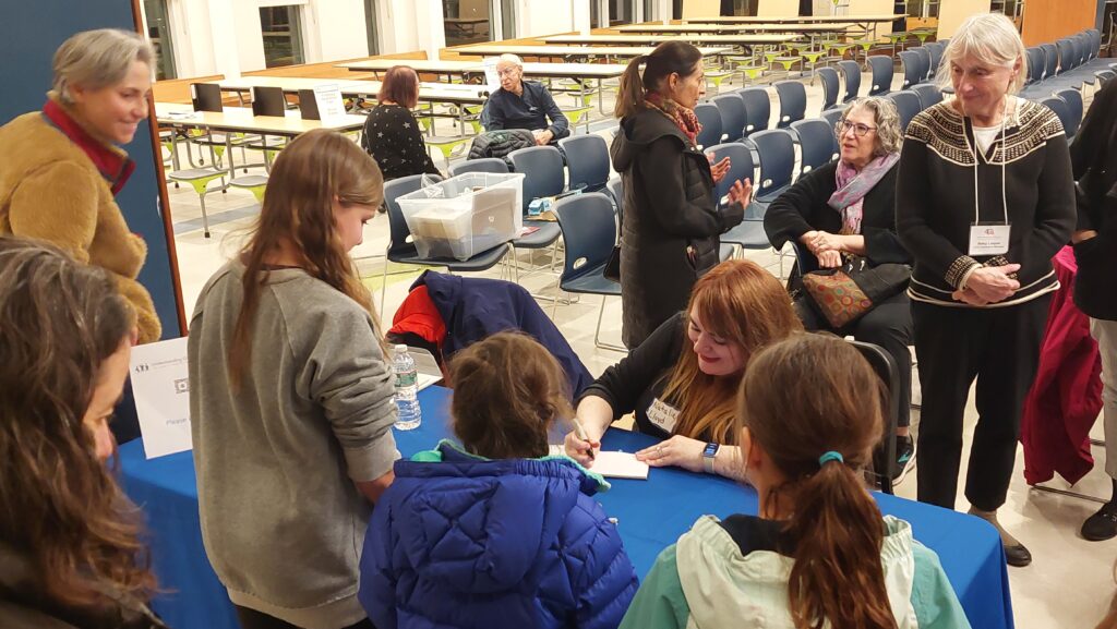 photo of Natalie Lloyd, Author of the book Hummingbird, sitting at a table, signing copies of her book while 3 girls wait and chat with her.